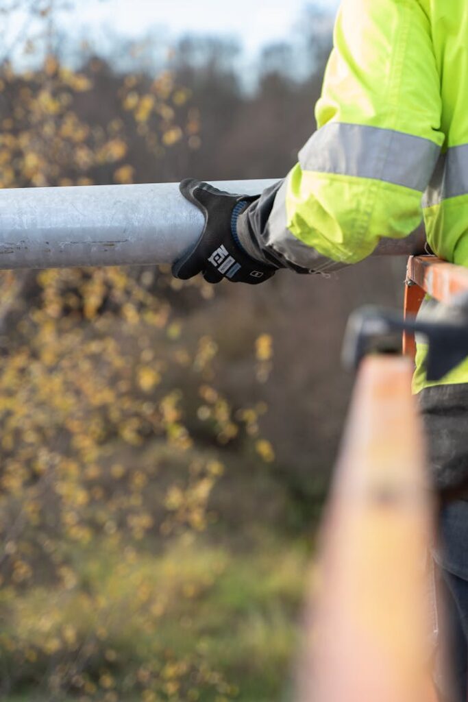 pexels-photo-13474295-1 Close-up of a construction worker holding a metal pipe outdoors with protective gear.
